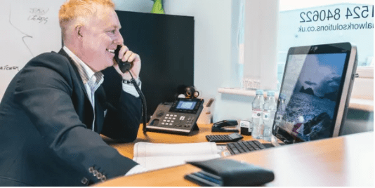 smiling recruitment consultant picking up phone in front of the computer